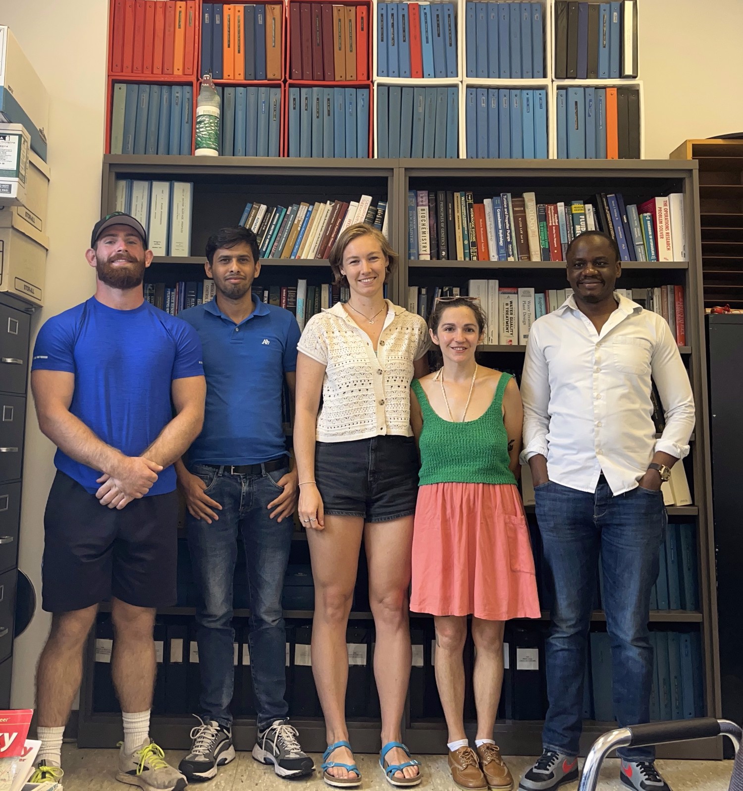 5 students standing in front of bookcase.