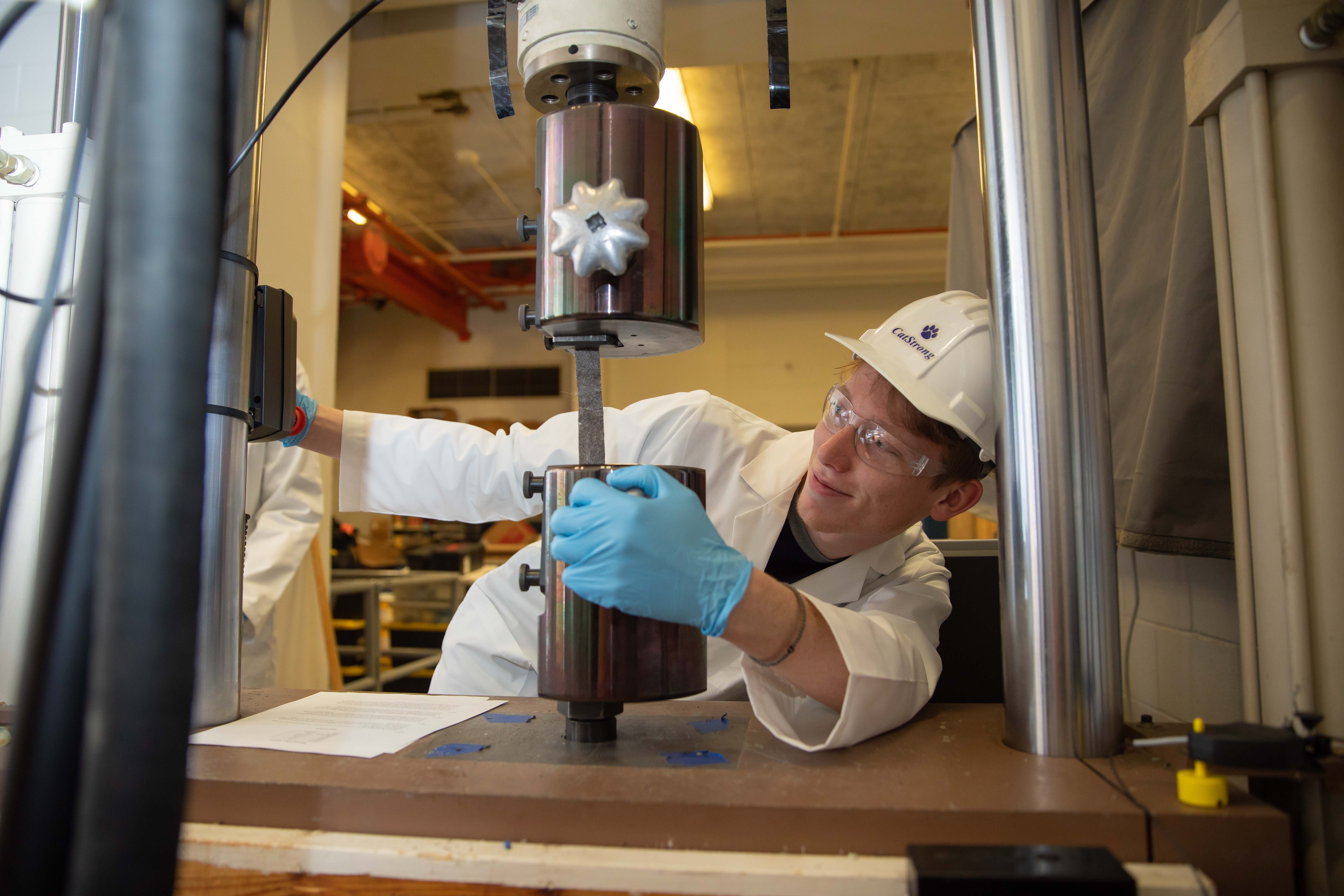 Photo of student testing a specimen of bio composite material made using human hair in tension using a Universal Testing Machine in the Structure’s lab. 