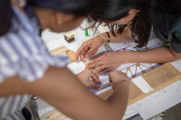 Two young women building a tower structure with wood craft materials.