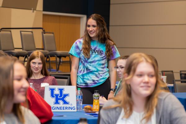 Student (female) with a tie-dyed SWE shirt standing at a table around a group of other female students.