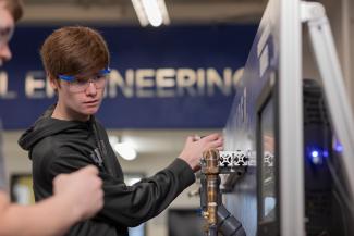 Student working on a copper pipe in with an engineering sign in the background.