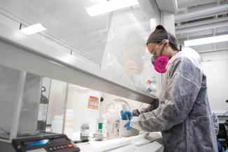 Researcher wearing a niosh mask and using a mortar and pestle.