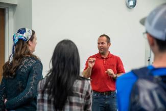 Group of students huddled around an alumni giving a lesson.