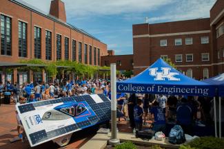 Freshman orientation happening outside in the Engineering courtyard with a solar car in the foreground and many groups of students in the background.