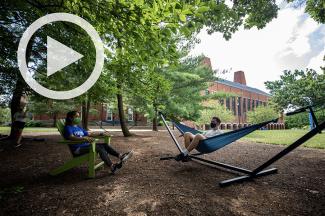 Two students lounging in a hammock and an adirondack chair.