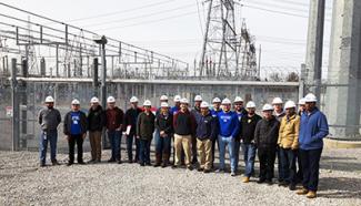 Group of people in hardhats standing near powerlines.