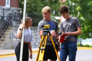 Three students with surveying machine practicing civil engineering