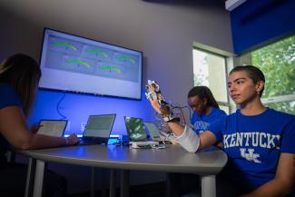 3 Students in front of a TV displaying images created from sensors that have been applied to a hand.