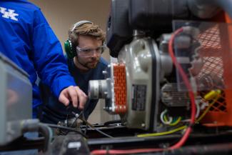 Student looking at an engine wearing safety glasses and headphones