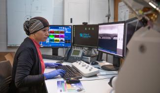 Student working in front of 4 monitors, wearing latex gloves and typing on a keyboard.