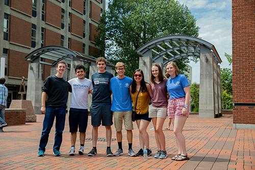 Group of 7 students, wearing shorts and t-shirts, standing in front of the Engineering Arches in the Engineering complex.