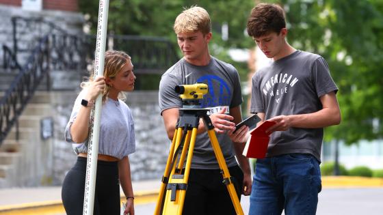 Three students with surveying machine practicing civil engineering