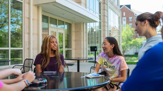 Students sitting outside at a table talking.