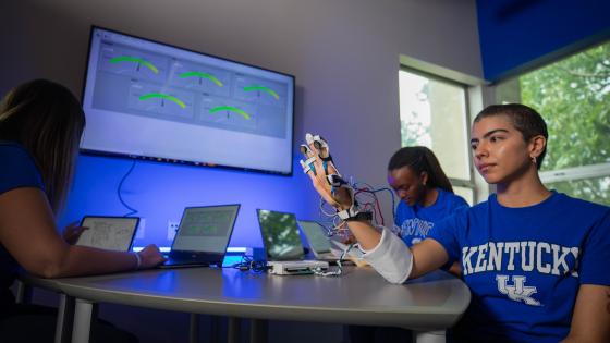 3 Students in front of a TV displaying images created from sensors that have been applied to a hand.