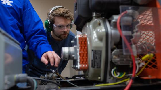 Student looking at an engine wearing safety glasses and headphones