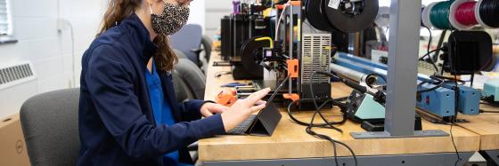 Student wearing a mask working on an iPad in a maker lab space.