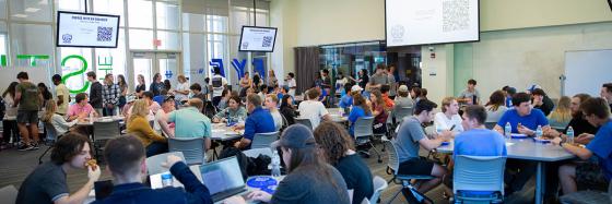 A classroom full of students sitting at tables and a projection screen that says "Engage with an engineer" at the front of the classroom.