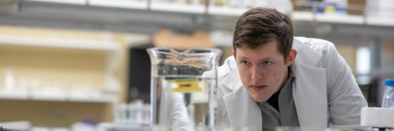 Student in a lab staring intently into a beaker full of clear liquid.