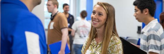 Student talking to a recruiter at a with other students milling around in the backgroud.