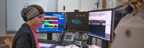 Student working in front of 4 monitors, wearing latex gloves and typing on a keyboard.