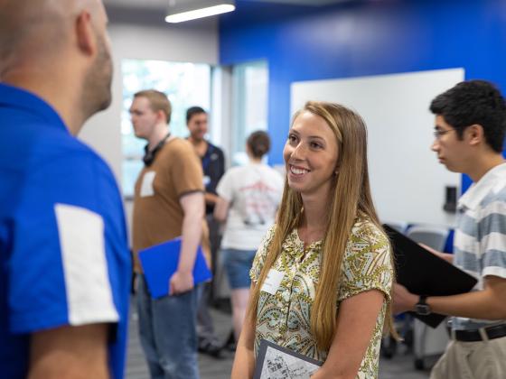 Student talking to a recruiter at a with other students milling around in the backgroud.